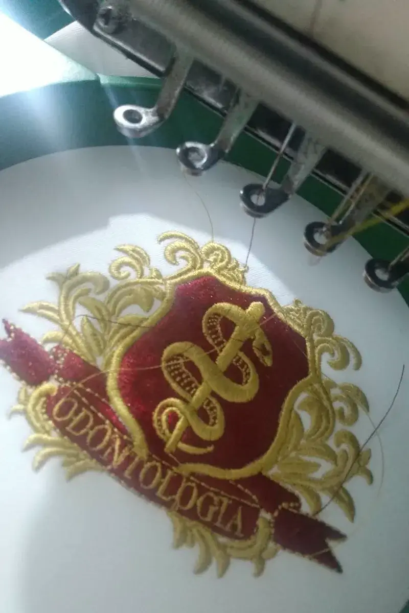Brasão de Odontologia sendo bordado em dourado e vinho na máquina